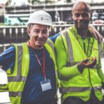 selective focus photography of two men standing side by side wearing green reflective vests