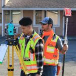 man in orange and yellow jacket holding blue and gray camera