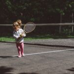 girl holding lawn tennis racket while standing beside white and black net